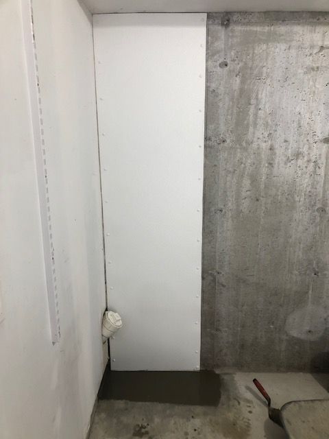 Narrow unfinished hallway corner with white and concrete walls, dark floor, and a broom handle on the ground