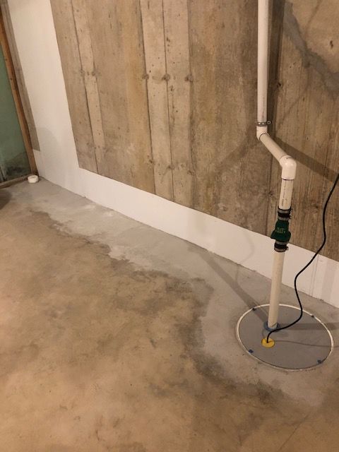 Basement floor with a vertical pipe and circular floor drain cover near a concrete wall