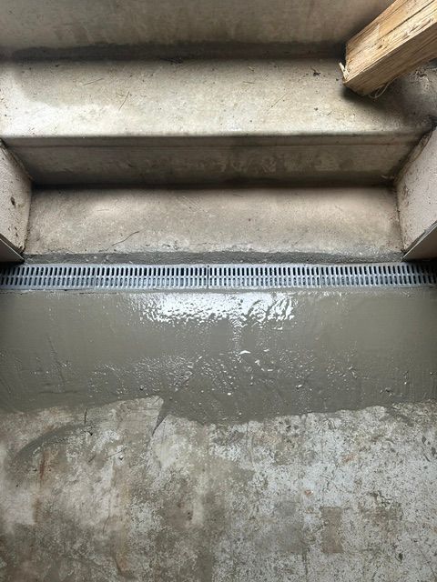 Wet concrete at the base of outdoor steps with a drainage grate.