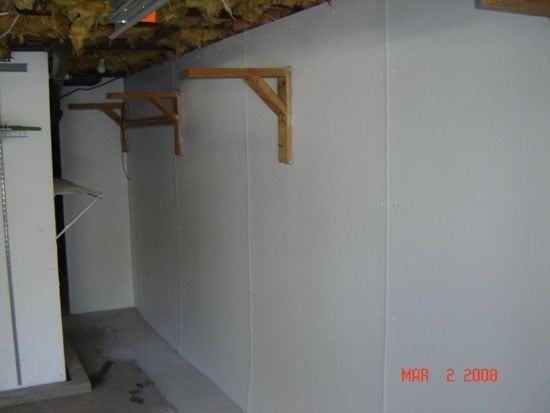 Empty basement room with white walls, exposed beams, and wooden wall brackets.