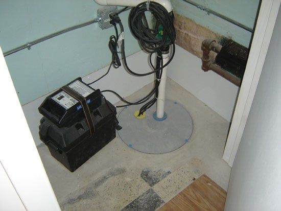 Basement utility area with coiled hoses, black equipment, and exposed pipes on a concrete floor.