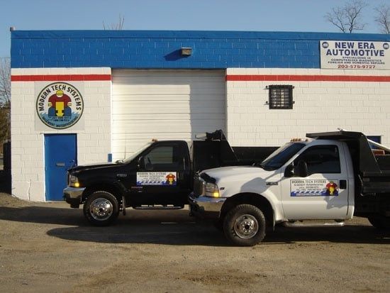 Two tow trucks parked outside a New Era Automotive building.