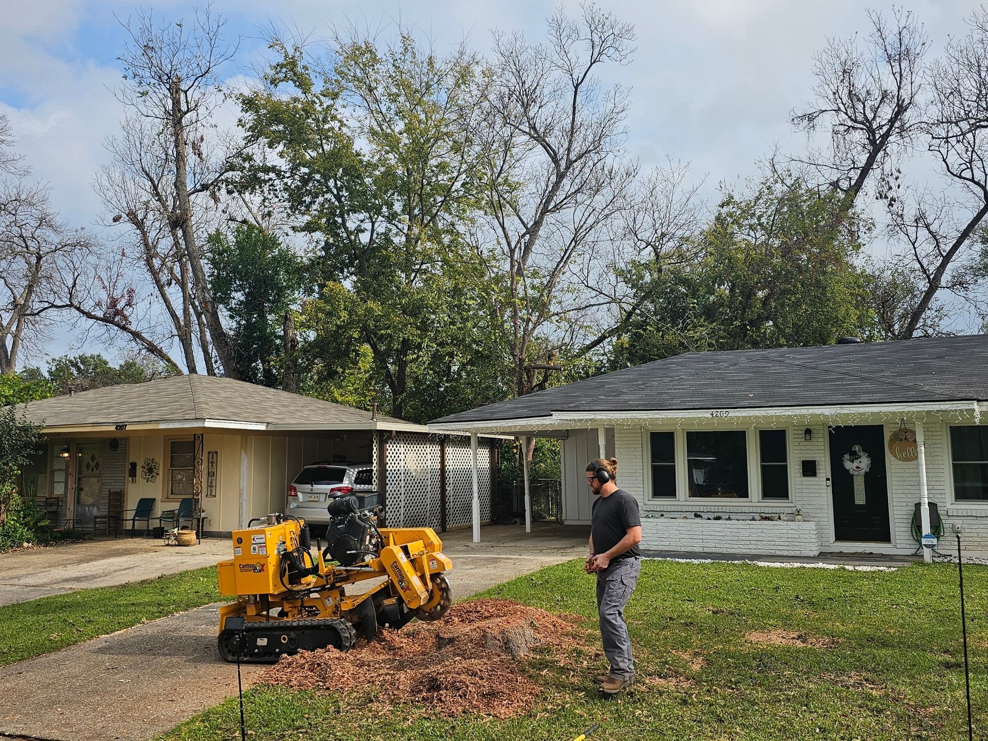 A man is working on a tree stump in front of a house.