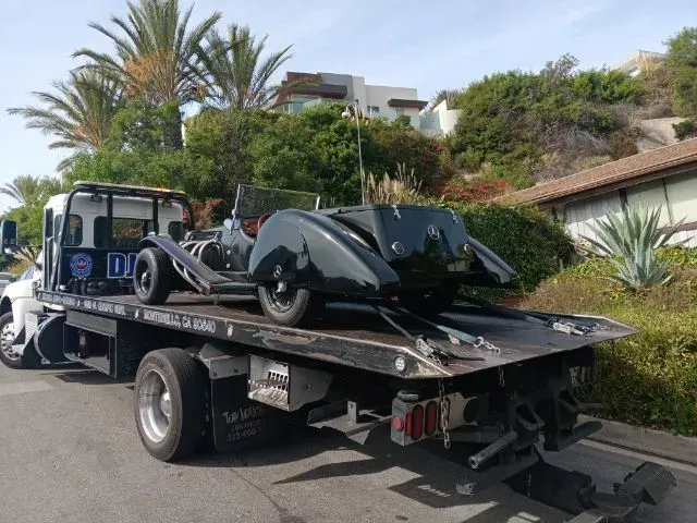 Red car being towed by a white tow truck on asphalt road; trees in the background.