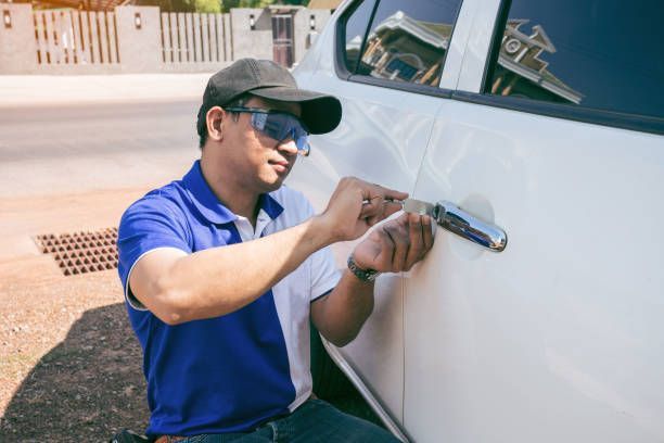 Person using tools to unlock a white car door, outside.