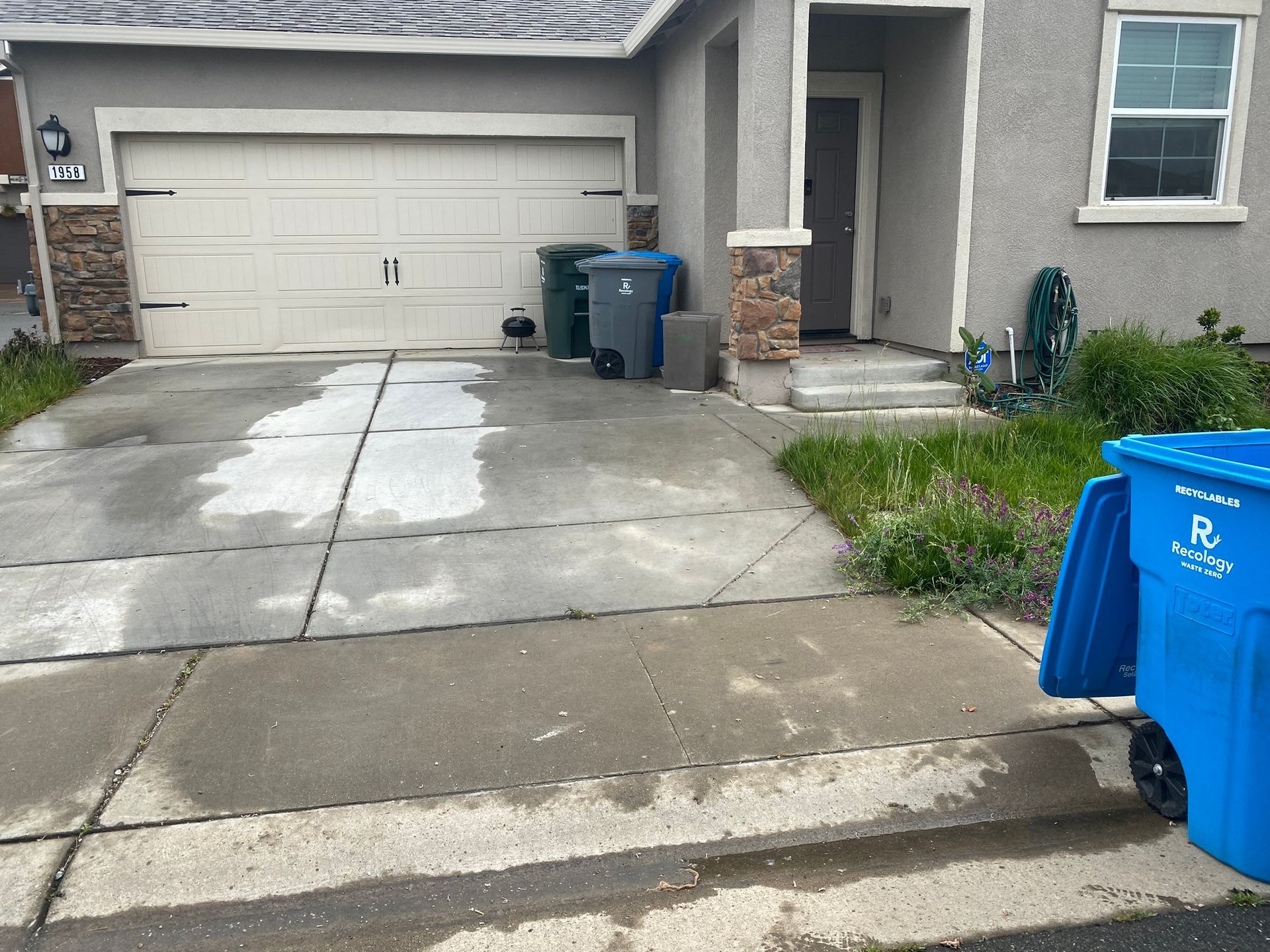 A blue trash can is parked in front of a house.