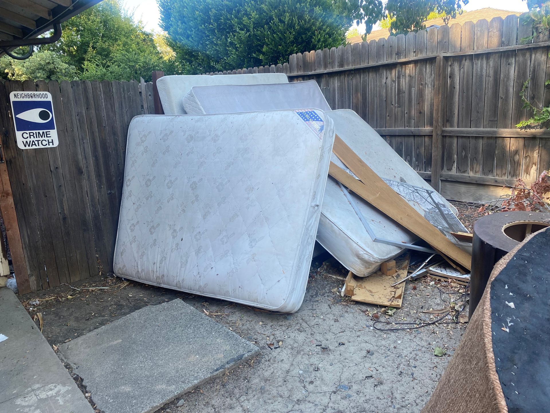 A pile of mattresses is sitting on the ground in front of a wooden fence.