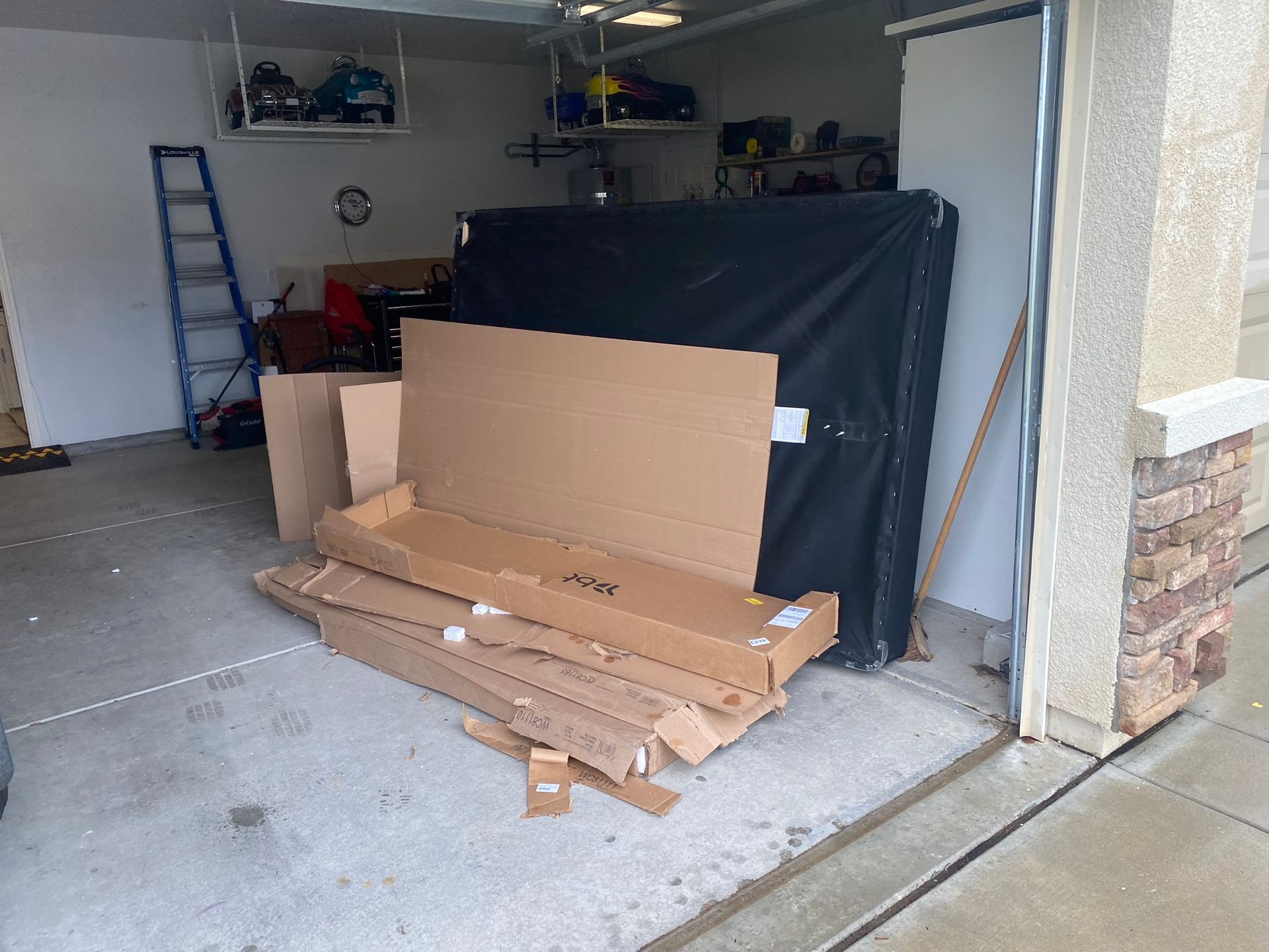 A pile of cardboard boxes in a garage next to a ladder.