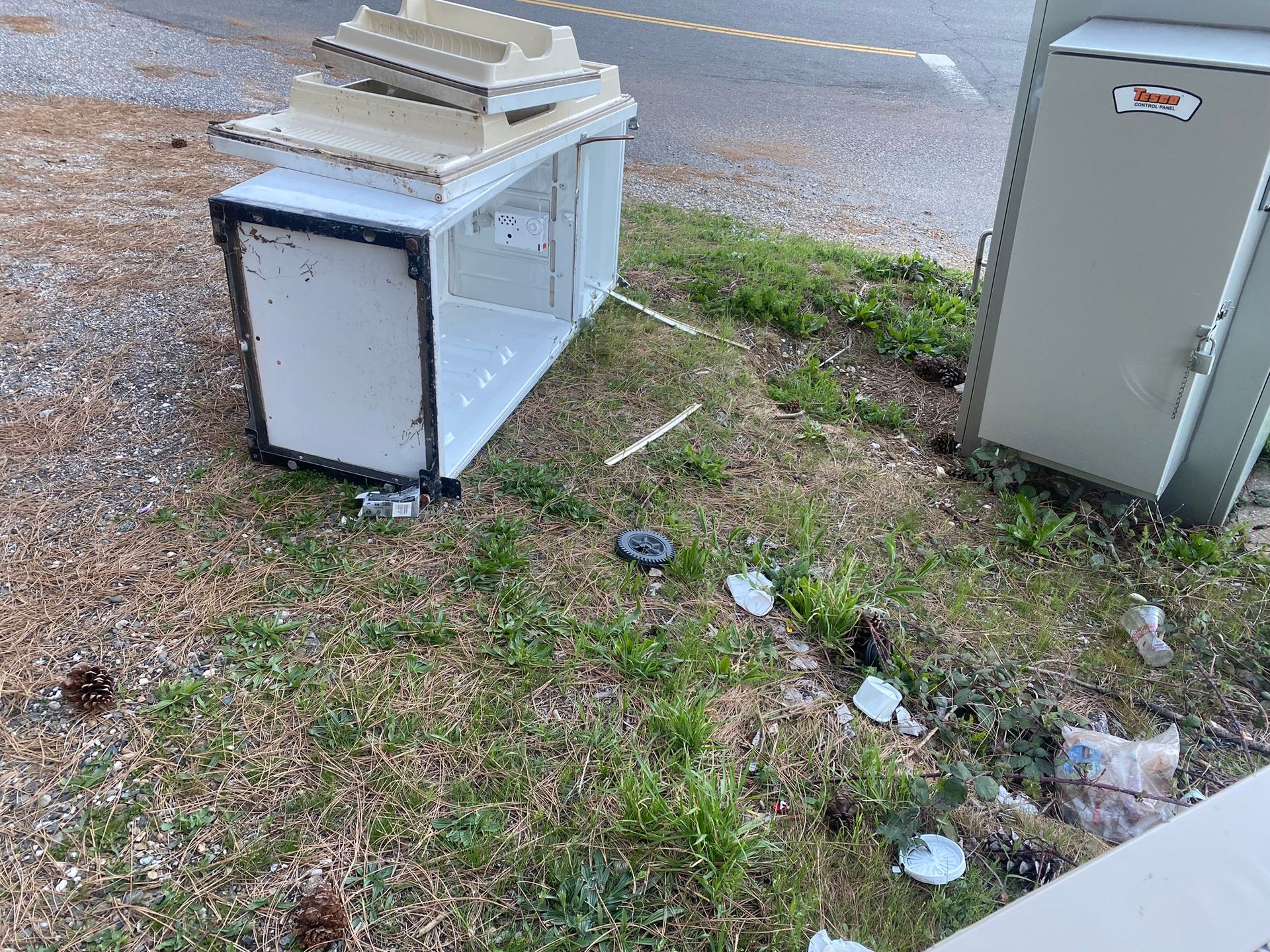 A trash can is sitting in the grass next to a building.