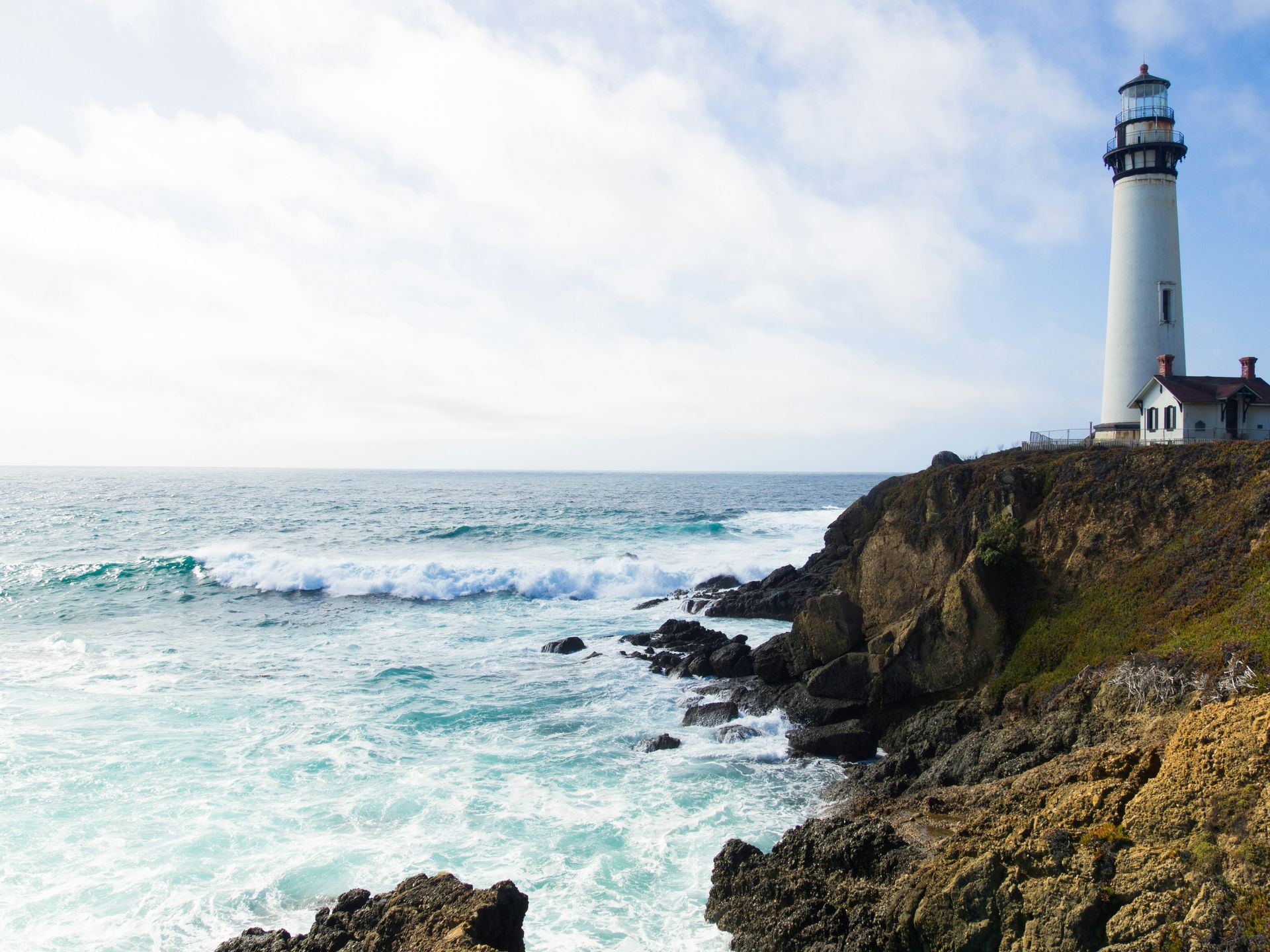 A lighthouse is sitting on top of a rocky cliff overlooking the ocean.