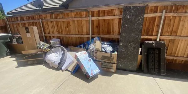 A bunch of boxes are sitting on the sidewalk in front of a wooden fence.