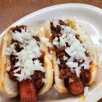 Two chili dogs topped with onions in a white bowl.