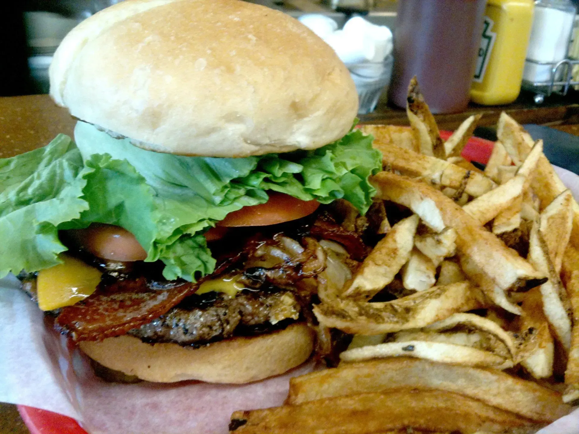 Burger with lettuce, tomato, bacon, cheese, and fries on a red-lined plate.