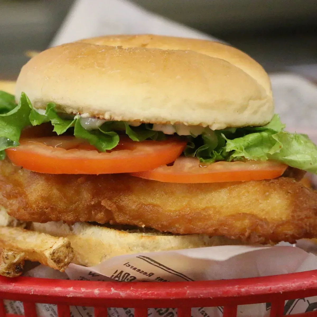 Fish sandwich with lettuce, tomato, and sauce on a bun, in a red basket.