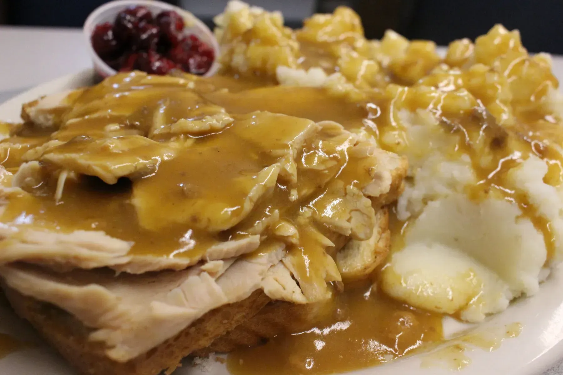 Turkey sandwich with gravy, mashed potatoes, and cranberry sauce on a white plate.