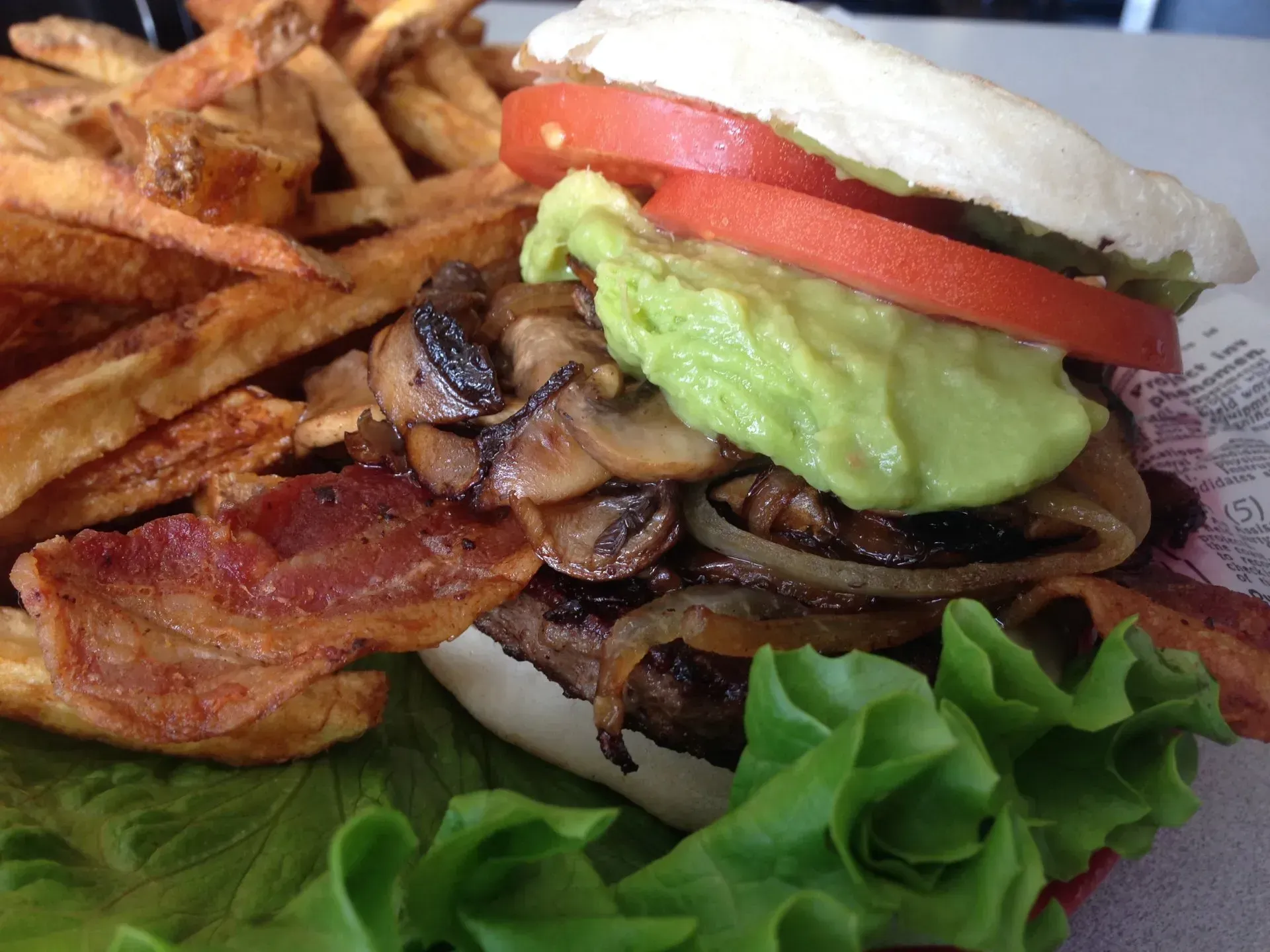 Burger with bacon, avocado, tomato, mushrooms, and fries.