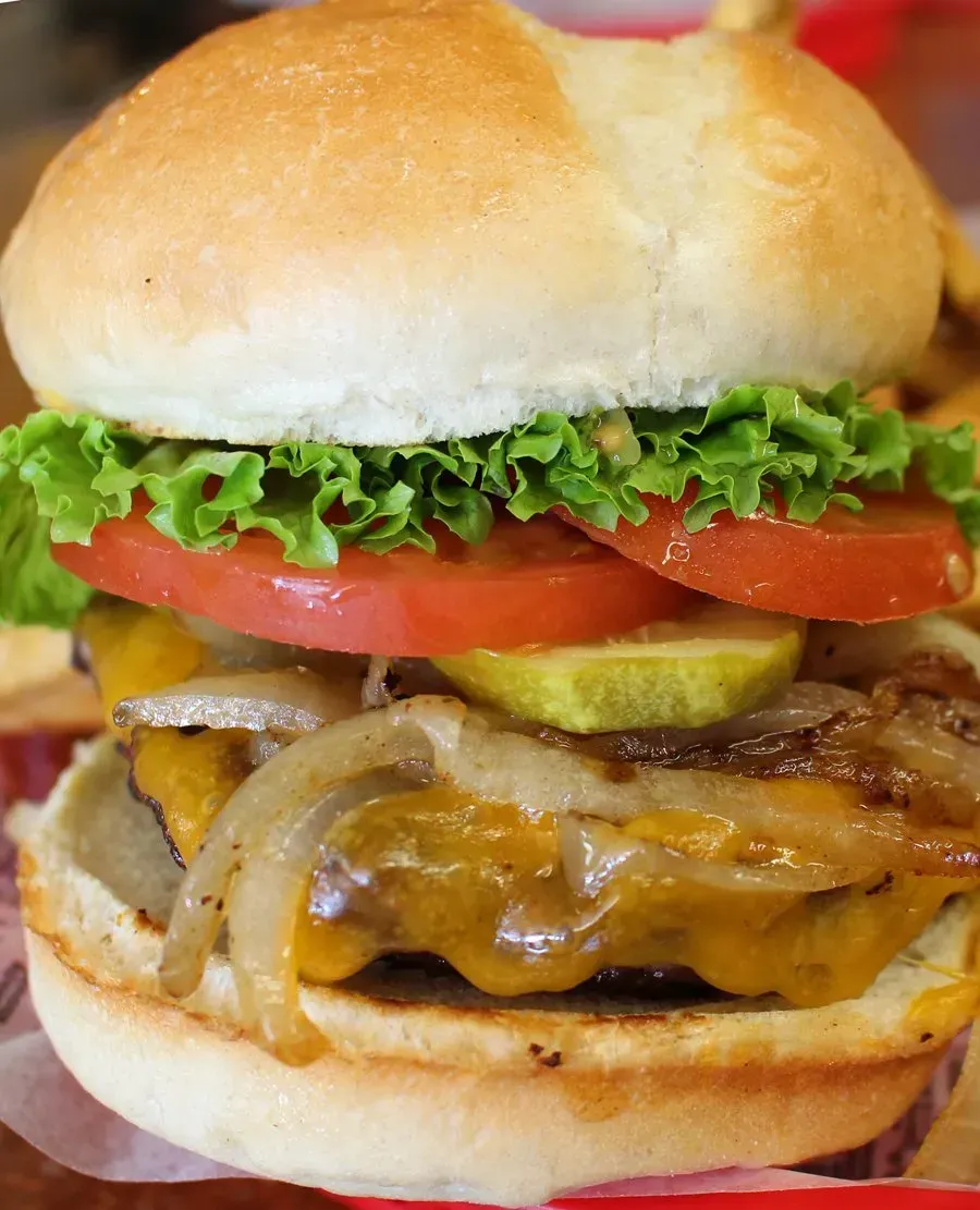 Cheeseburger with lettuce, tomato, pickle, and caramelized onions on a bun.