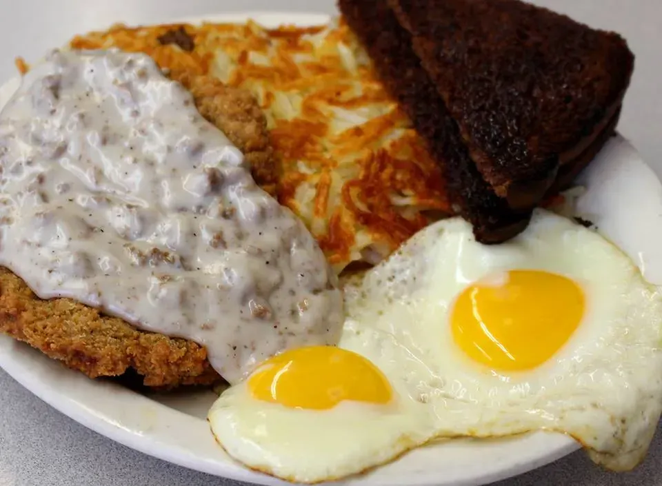 Plate with fried chicken covered in gravy, hash browns, toast, and two fried eggs.