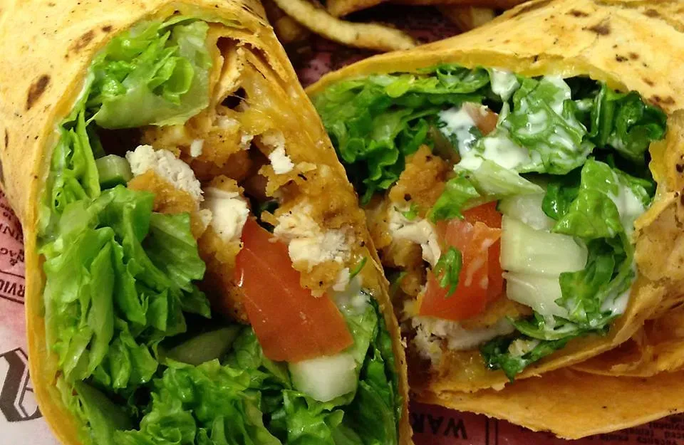 Chicken wrap cut in half; romaine lettuce, tomato, creamy dressing, and chicken inside.
