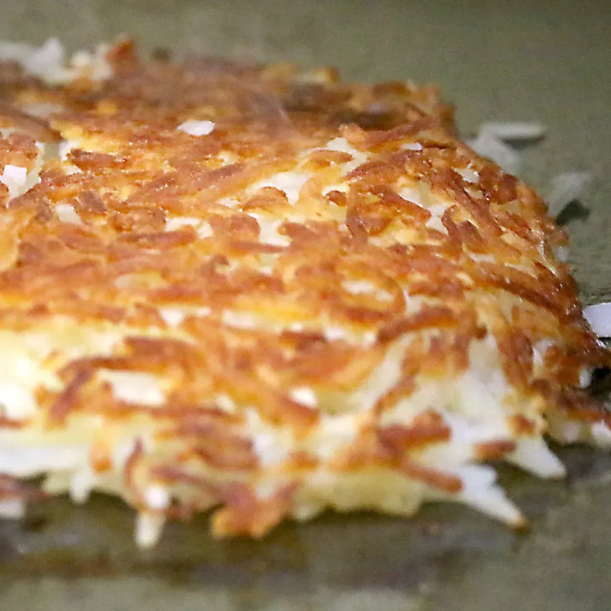 Crispy, golden-brown hash browns cooking on a griddle, showing shredded potato texture.