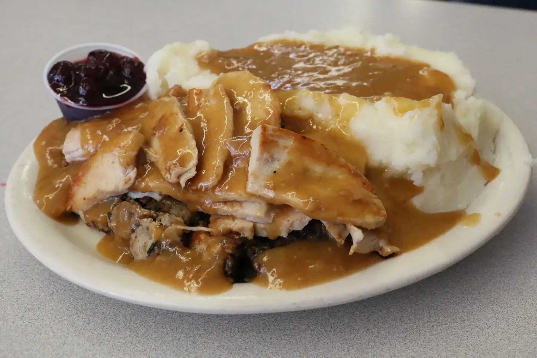 Plate of turkey slices, mashed potatoes with gravy, stuffing, and cranberry sauce.