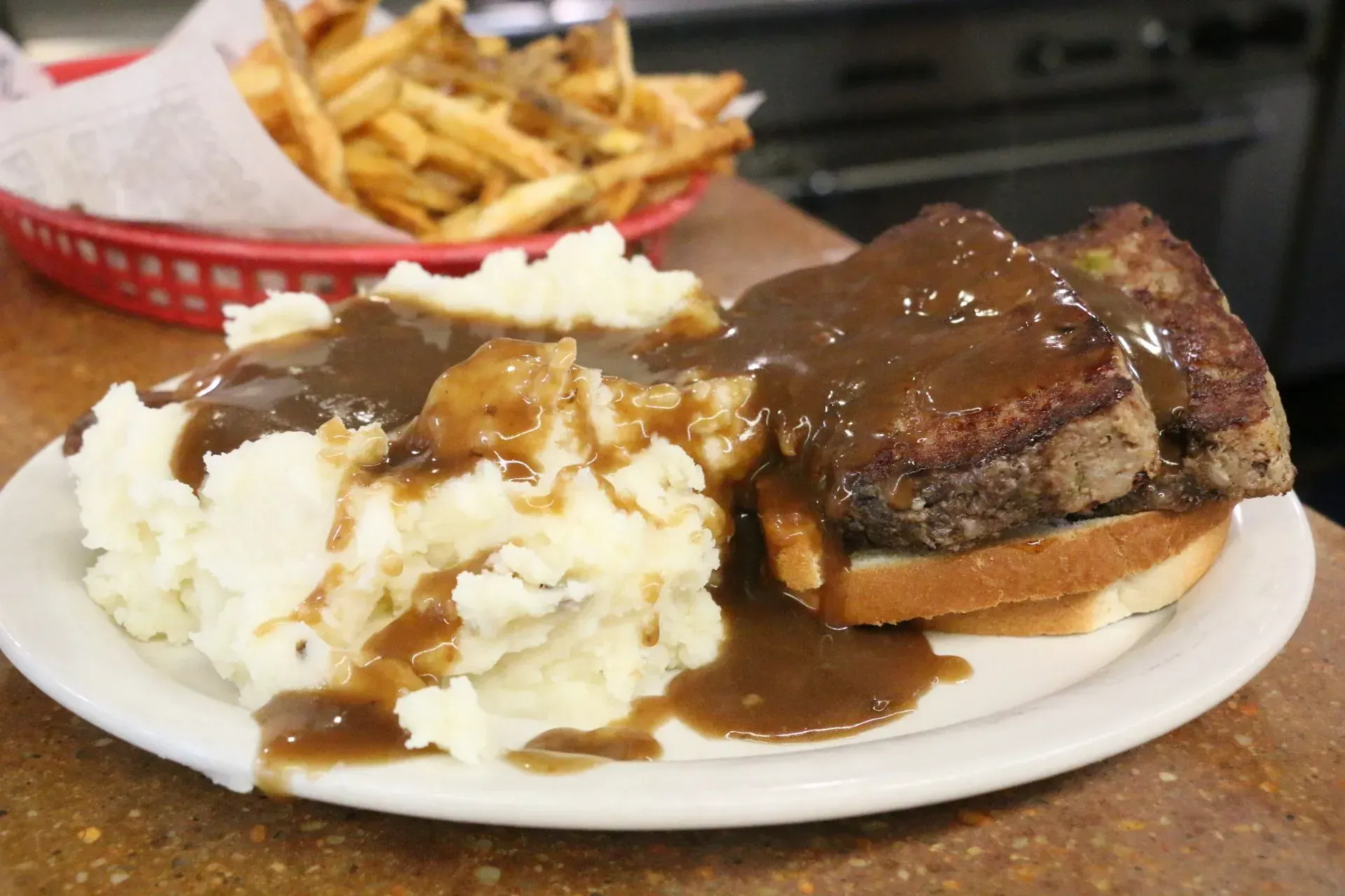 Plate of mashed potatoes, gravy, and roast beef sandwich with fries in background.