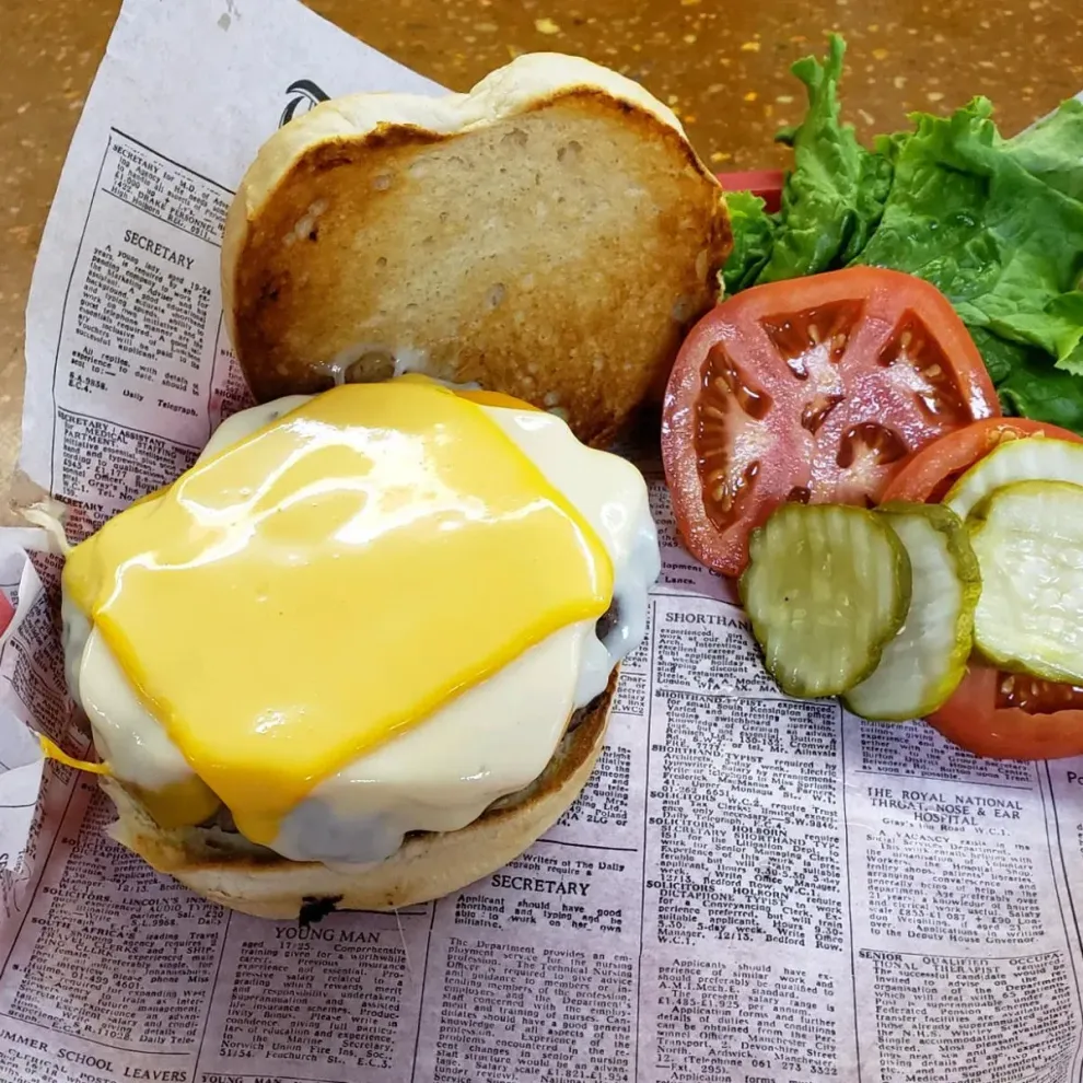 Cheeseburger with melted cheese on a toasted bun, accompanied by tomato slices, pickles, and lettuce.