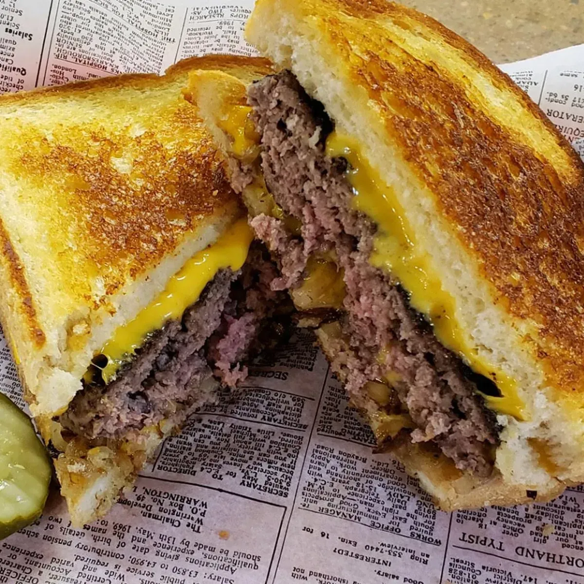 Grilled cheese burger, cut in half, with melted cheese and patty between toasted bread.