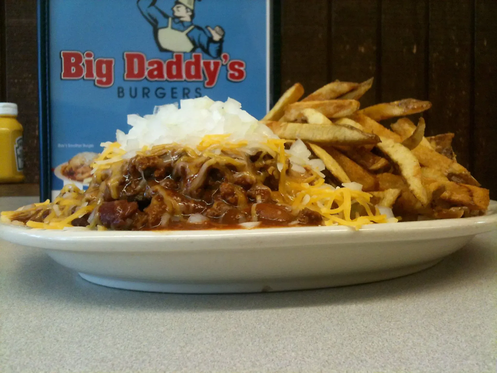 Plate of chili cheese fries topped with onions, in front of a Big Daddy's Burgers sign.
