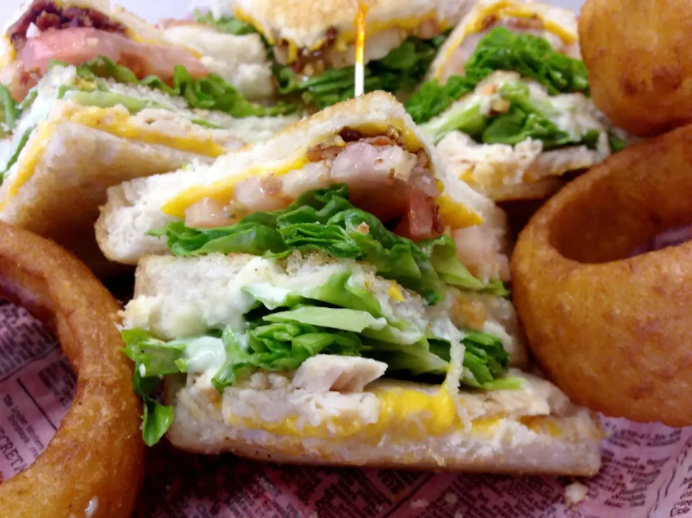 Club sandwich with lettuce, tomato, bacon, and onion rings.
