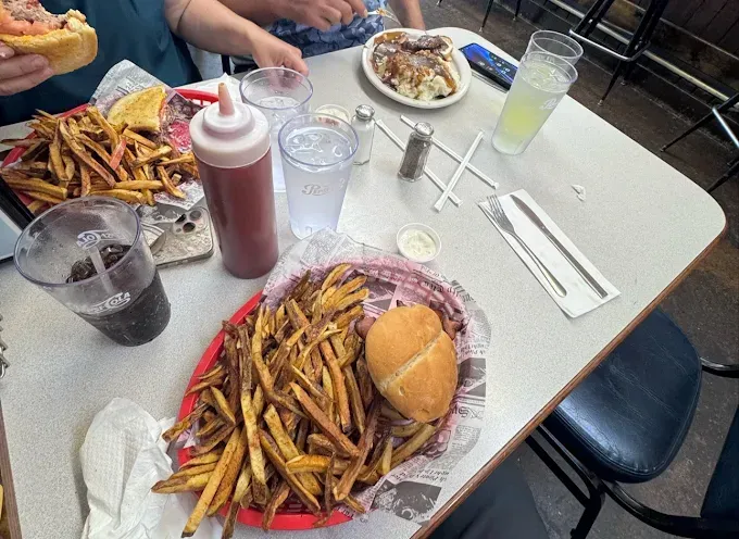 Table of food with fries, burger, drinks, and ketchup. People eating at a diner, likely lunch.