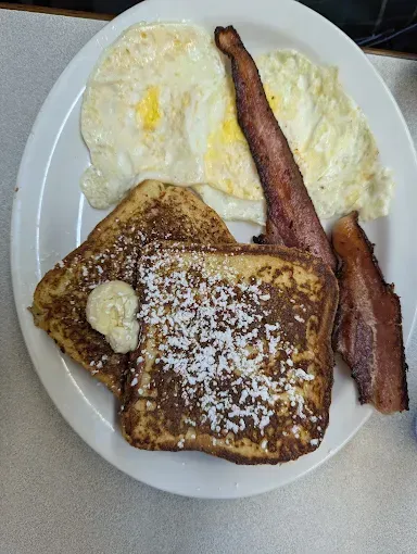 Breakfast plate: French toast with powdered sugar and butter, two fried eggs, bacon.