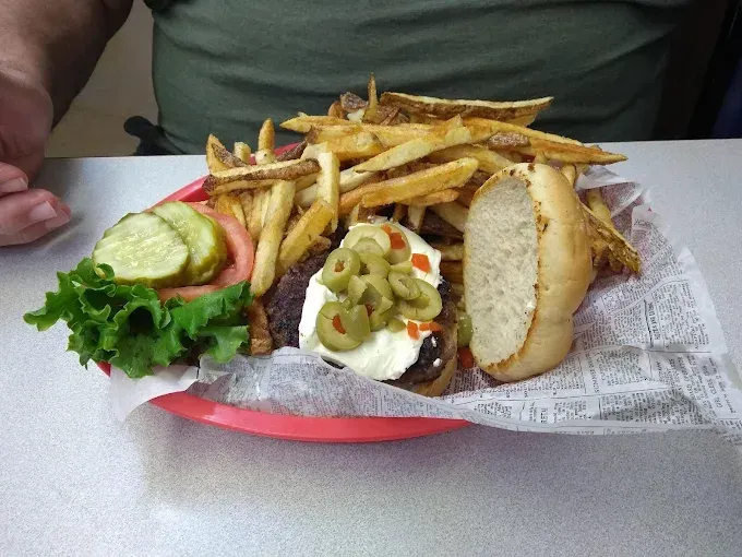 Plate of burger, fries, and pickles on newspaper.
