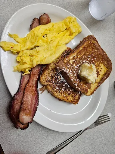 Breakfast plate: Scrambled eggs, bacon, French toast with butter and powdered sugar.