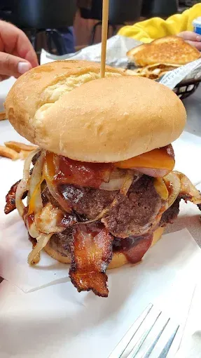Large burger with bacon, onions, and cheese on a bun, held together with a skewer.