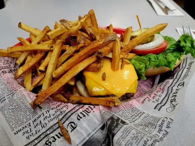 Burger with cheese, fries, lettuce, tomato, onion and pickle on a paper-lined basket.