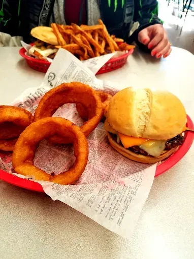Burger with cheese, onion rings, and fries in red baskets on a table.