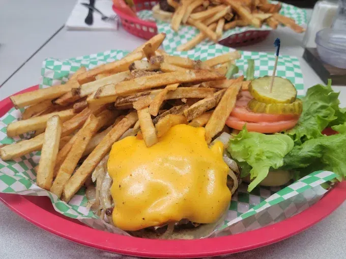 Cheeseburger with fries in a red basket, topped with lettuce, tomato, and a pickle.