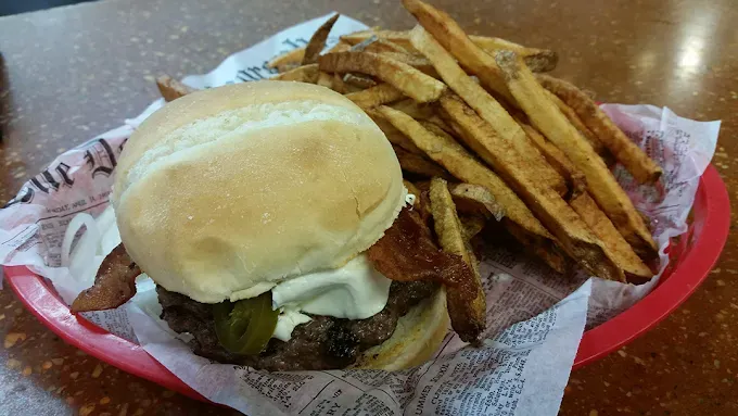 Hamburger with bacon, pickles, and fries in a basket.