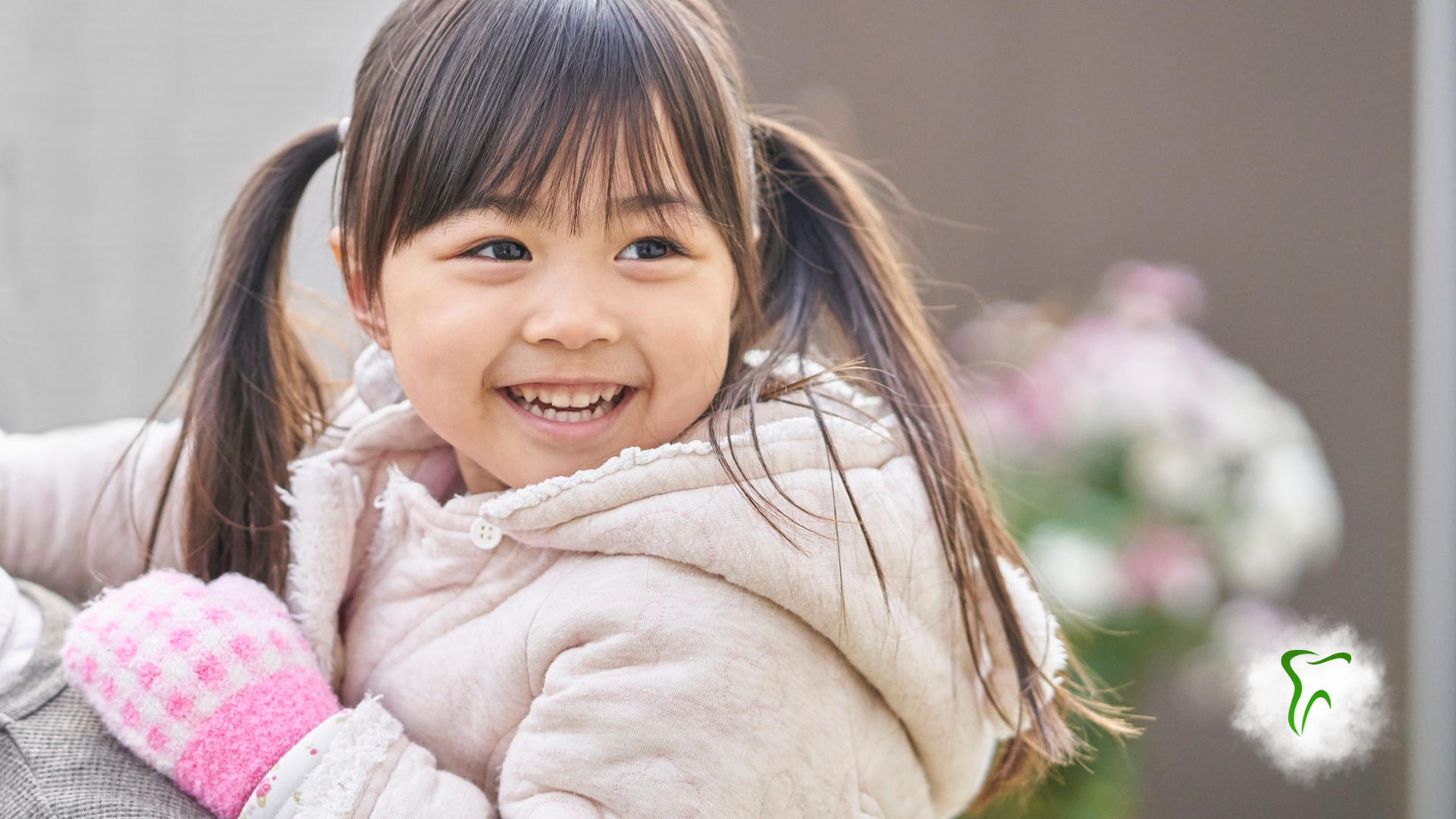 Girl in pink mittens smiles, wearing a cream coat.