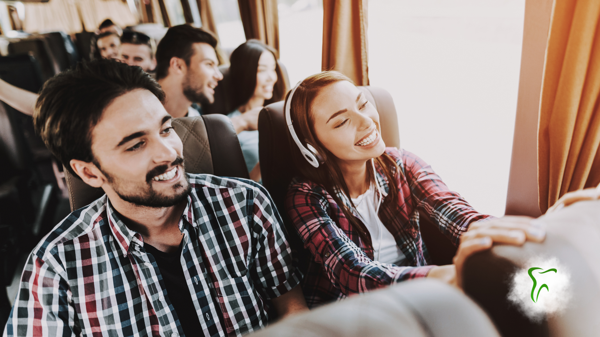 People smiling on a bus. A woman wears headphones. The man next to her smiles. They sit by a window.