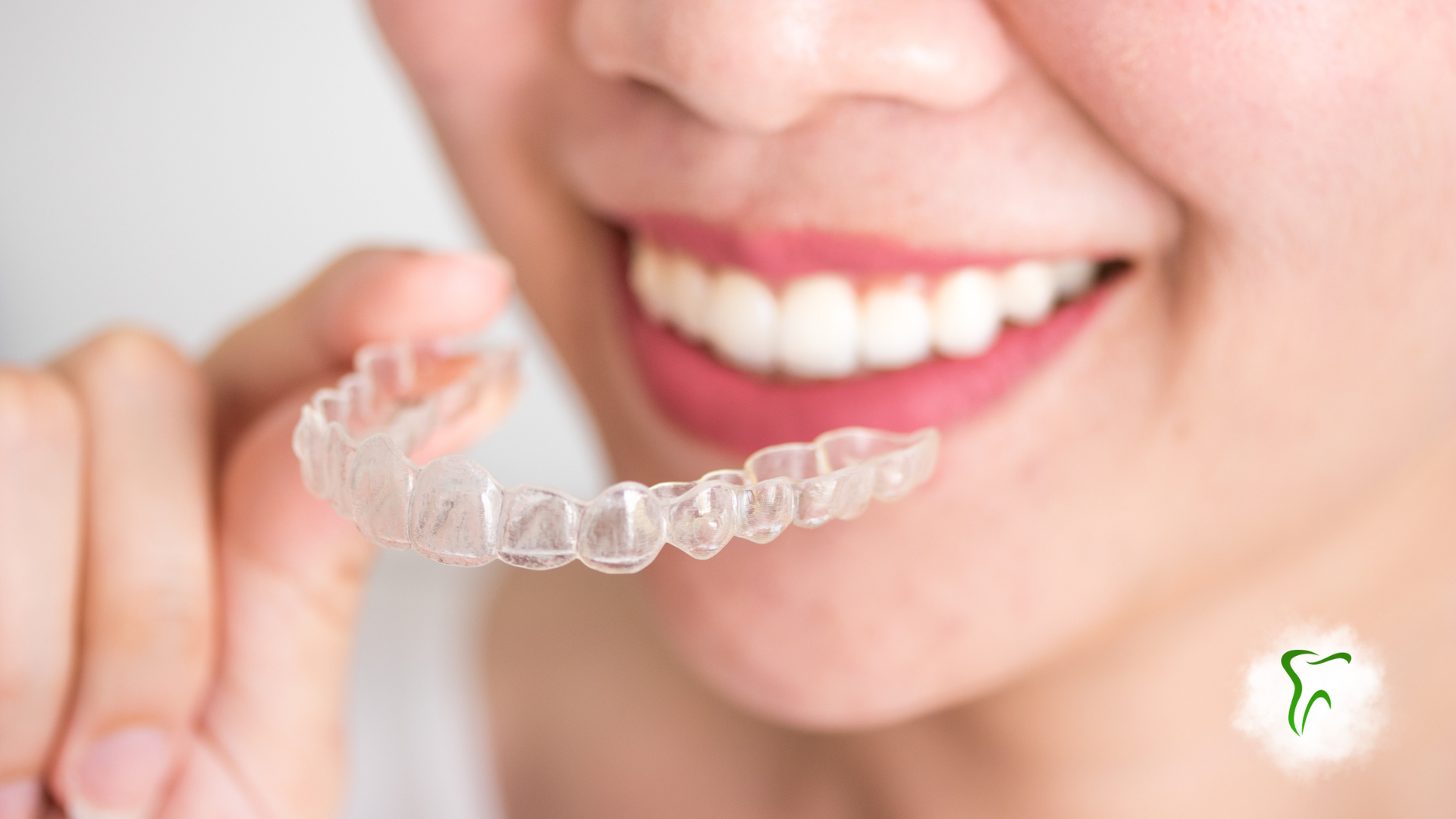 Person holding clear aligner, smiling, preparing to put it in mouth.