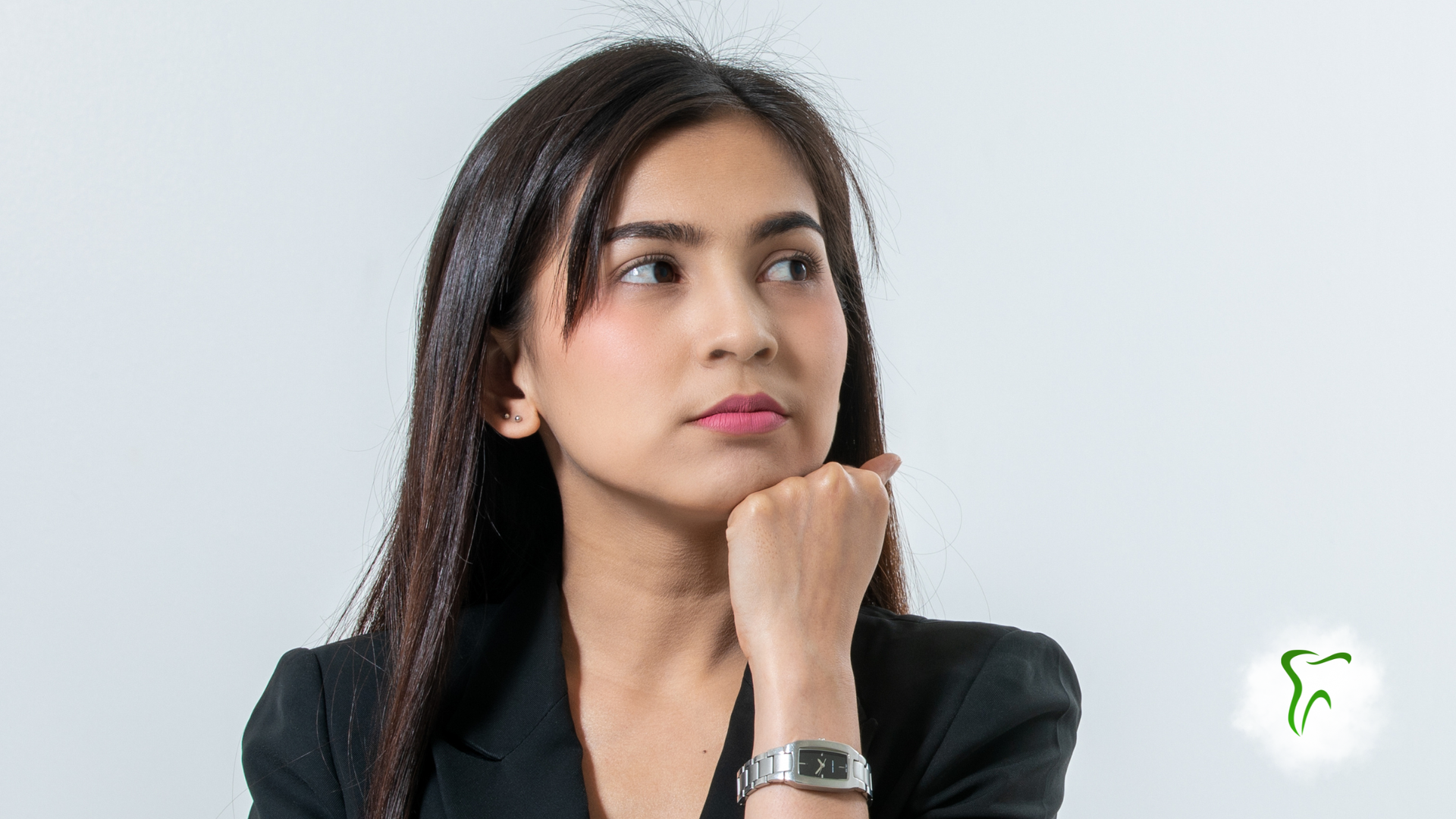 Woman in a black blazer, looking thoughtfully to the side, chin resting on hand. White background.