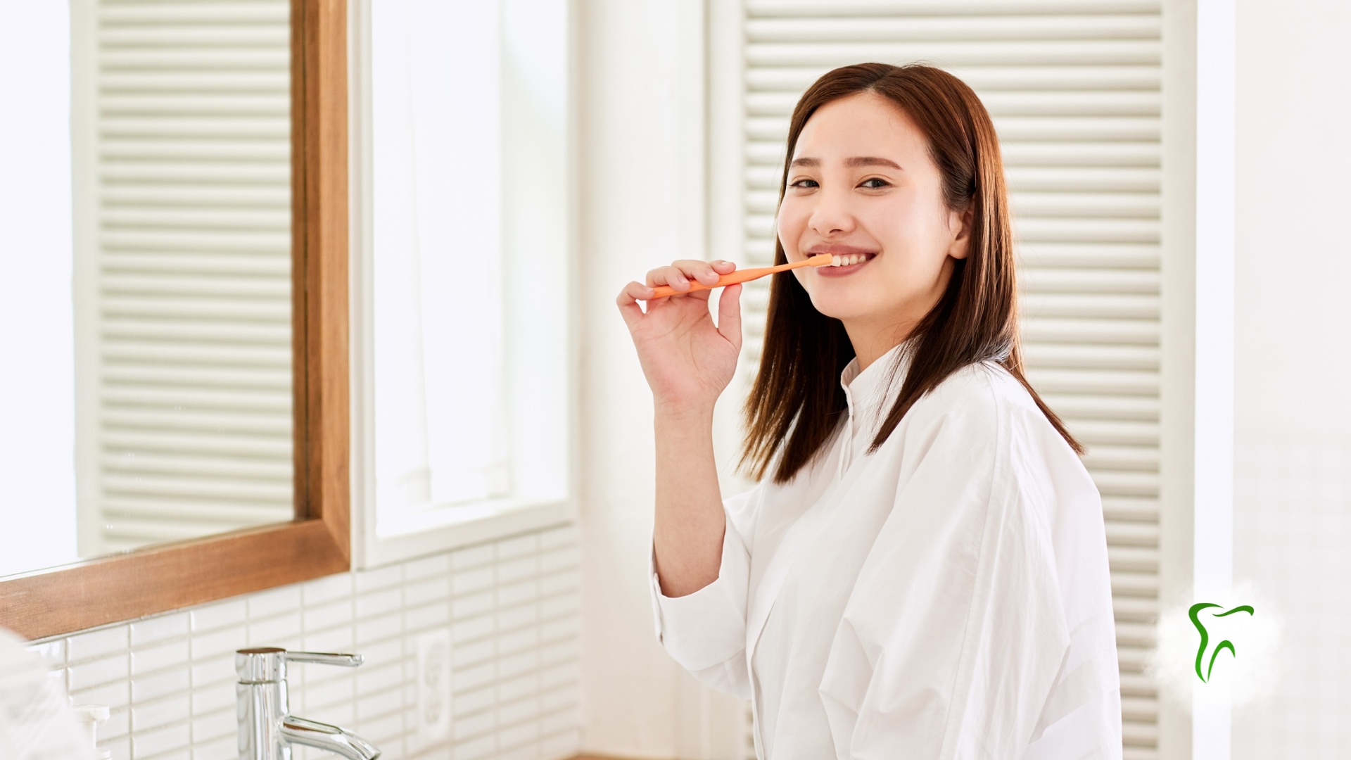 Woman brushing teeth in bathroom, smiling, facing mirror.