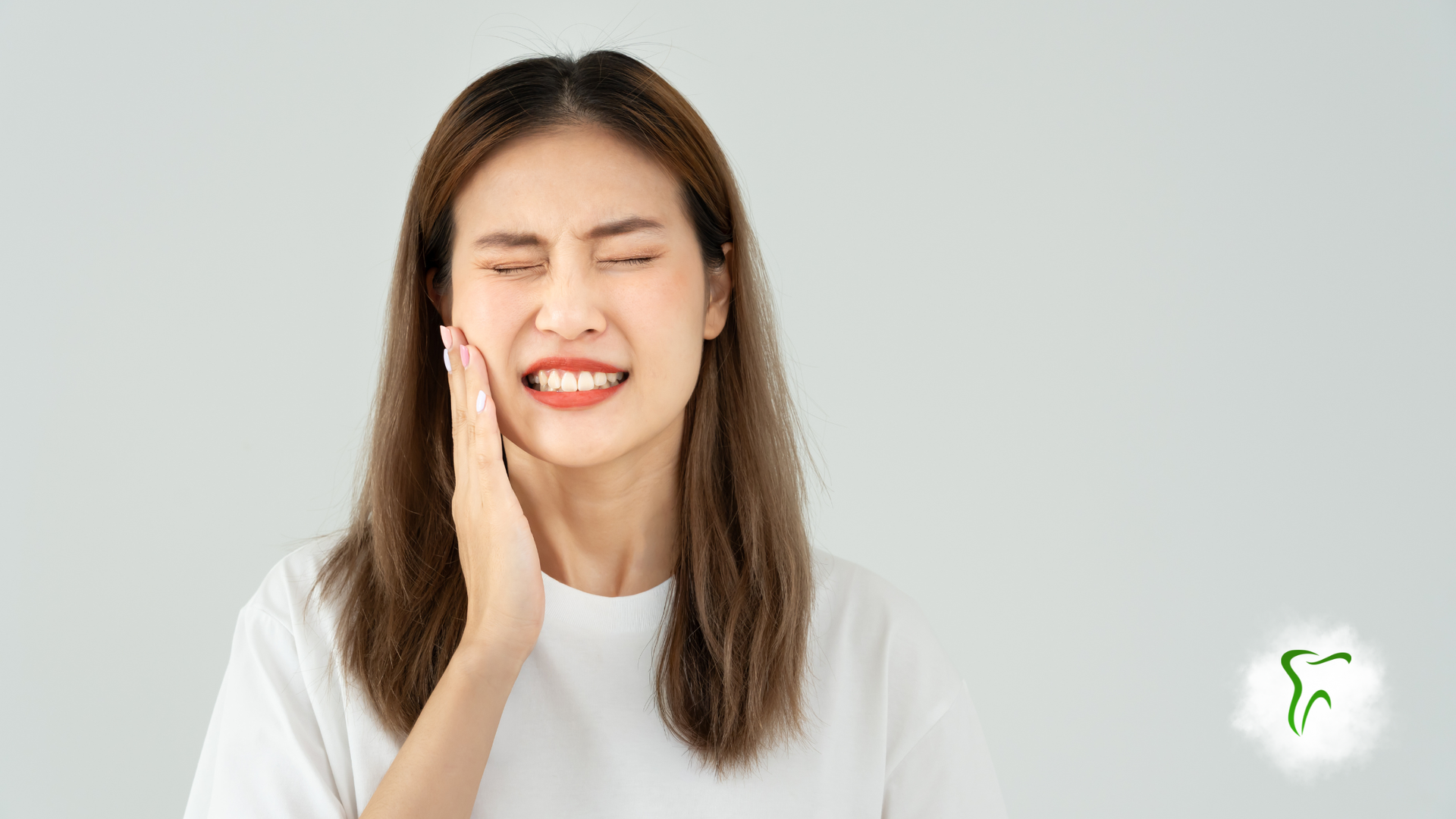 Woman holding her cheek in pain, likely from a toothache, against a white backdrop.