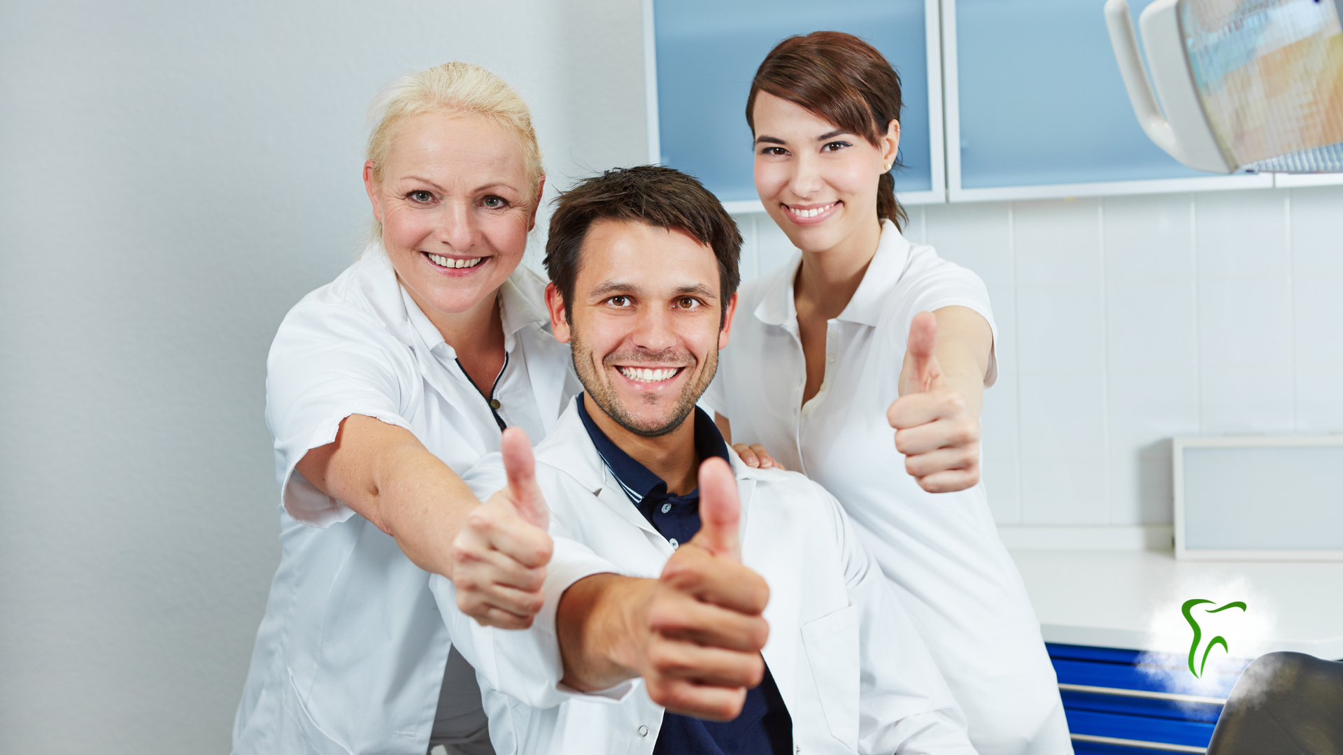Three smiling dental professionals giving thumbs up in a dental office.
