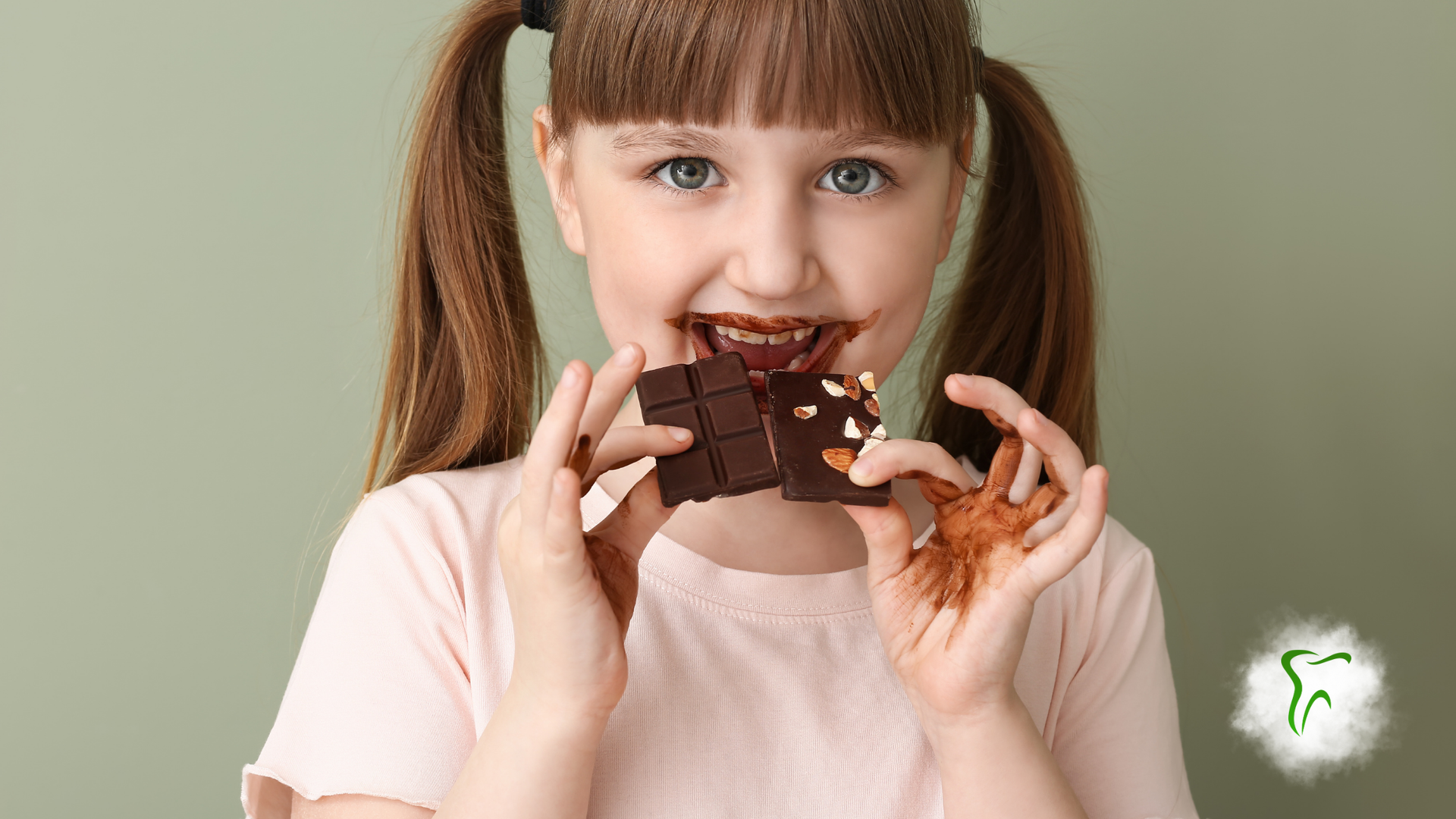 Girl with pigtails eating a chocolate bar, chocolate on her hands and mouth, green background.