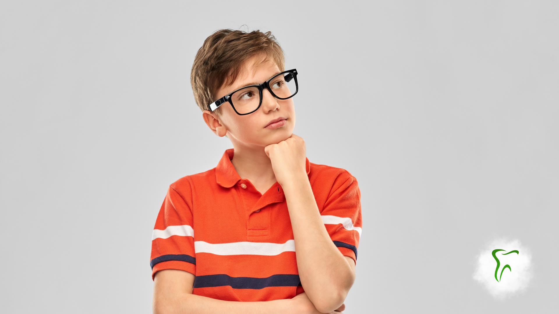 Boy in orange shirt and glasses, hand on chin, looking up thoughtfully.