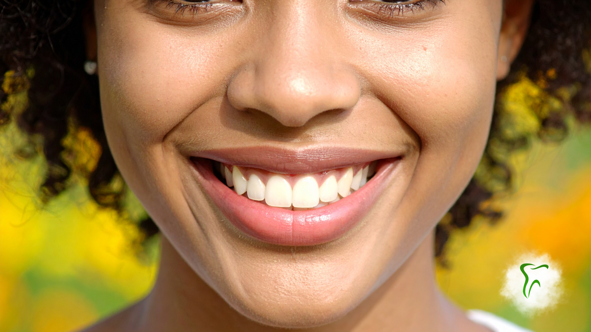 Close-up of a person's mouth, showing slightly discolored teeth and a mole on the chin.