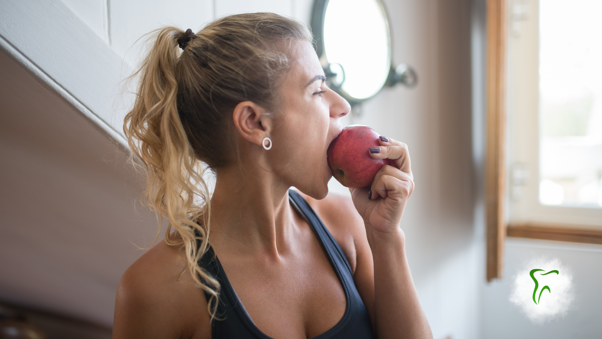 Woman in athletic wear biting into a red apple. Blonde hair pulled back, natural light.